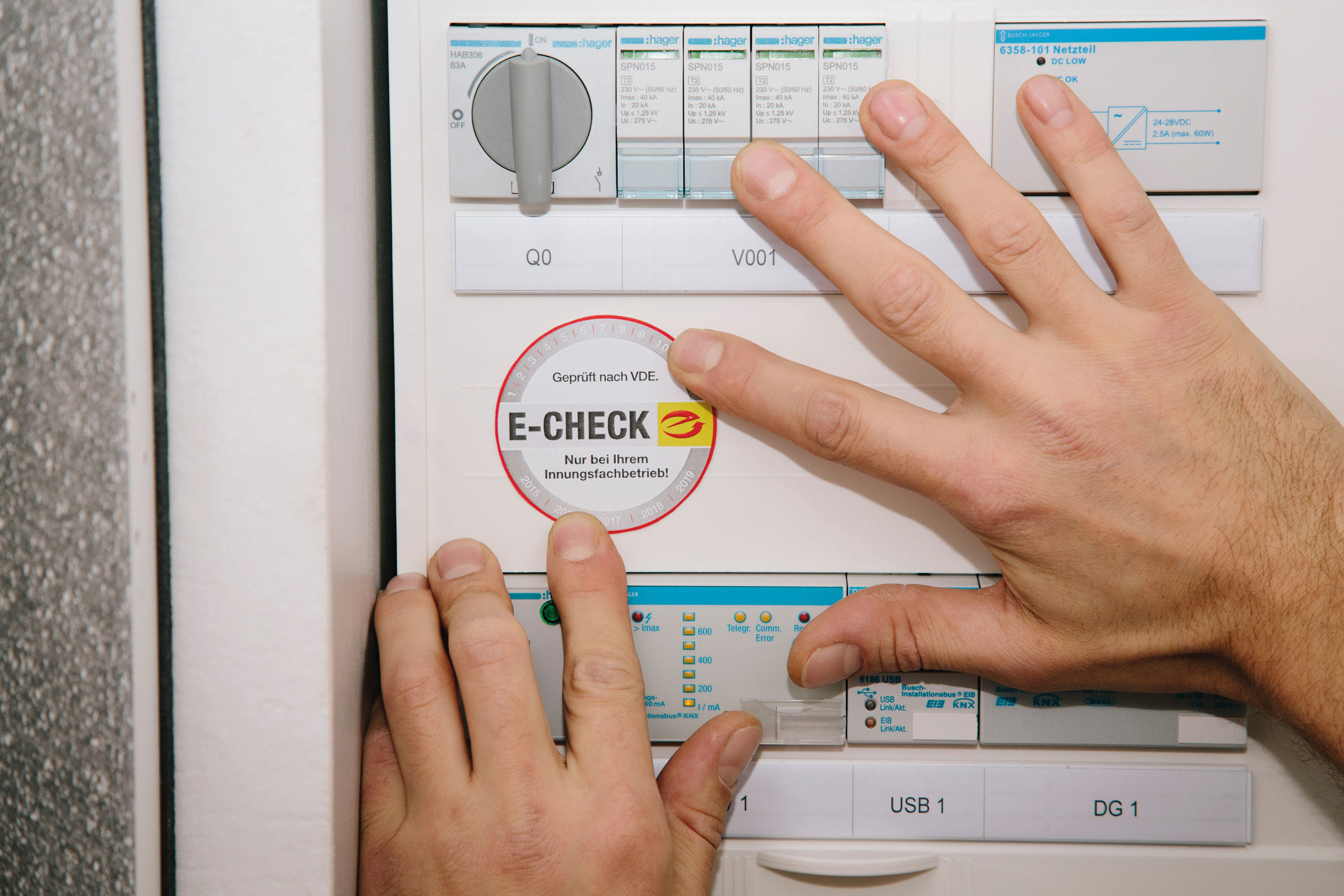 Zwei Hände kleben einen E-Check Aufkleber in den Sicherungskasten