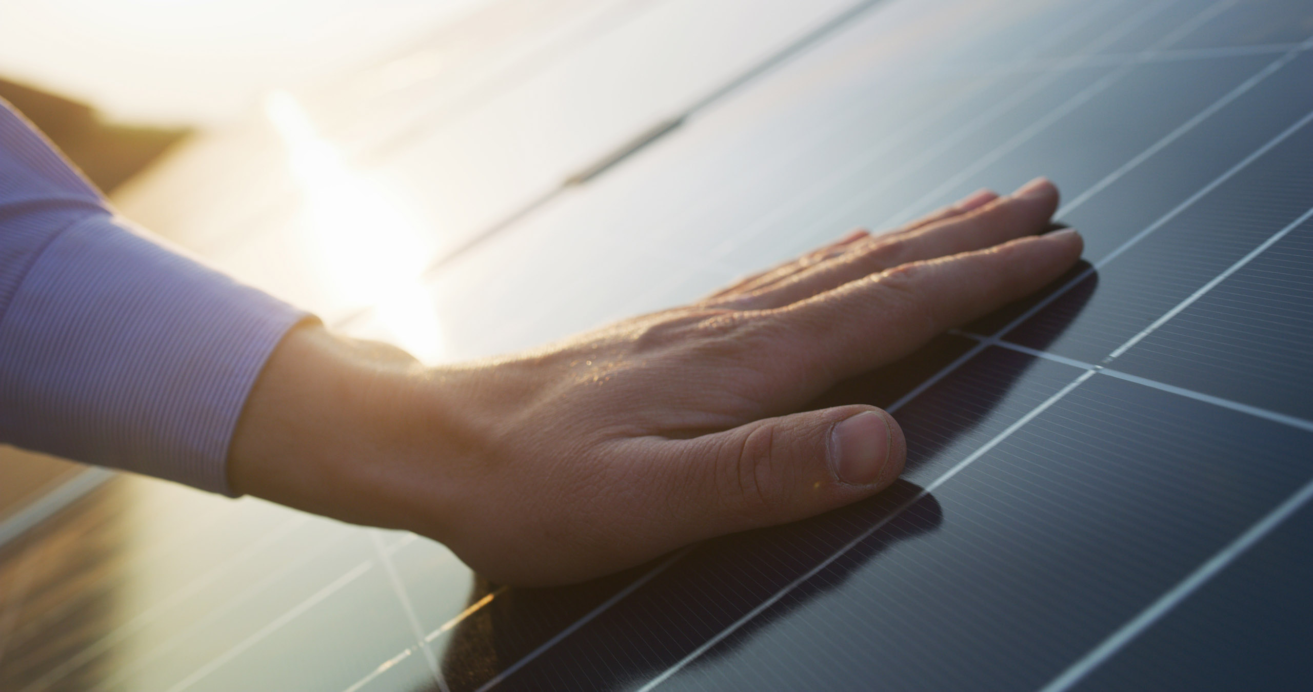 Nahaufnahme der Hand eines jungen Ingenieurs, der bei Sonnenuntergang die Funktion und Sauberkeit von Photovoltaik-Solarmodulen überprüft