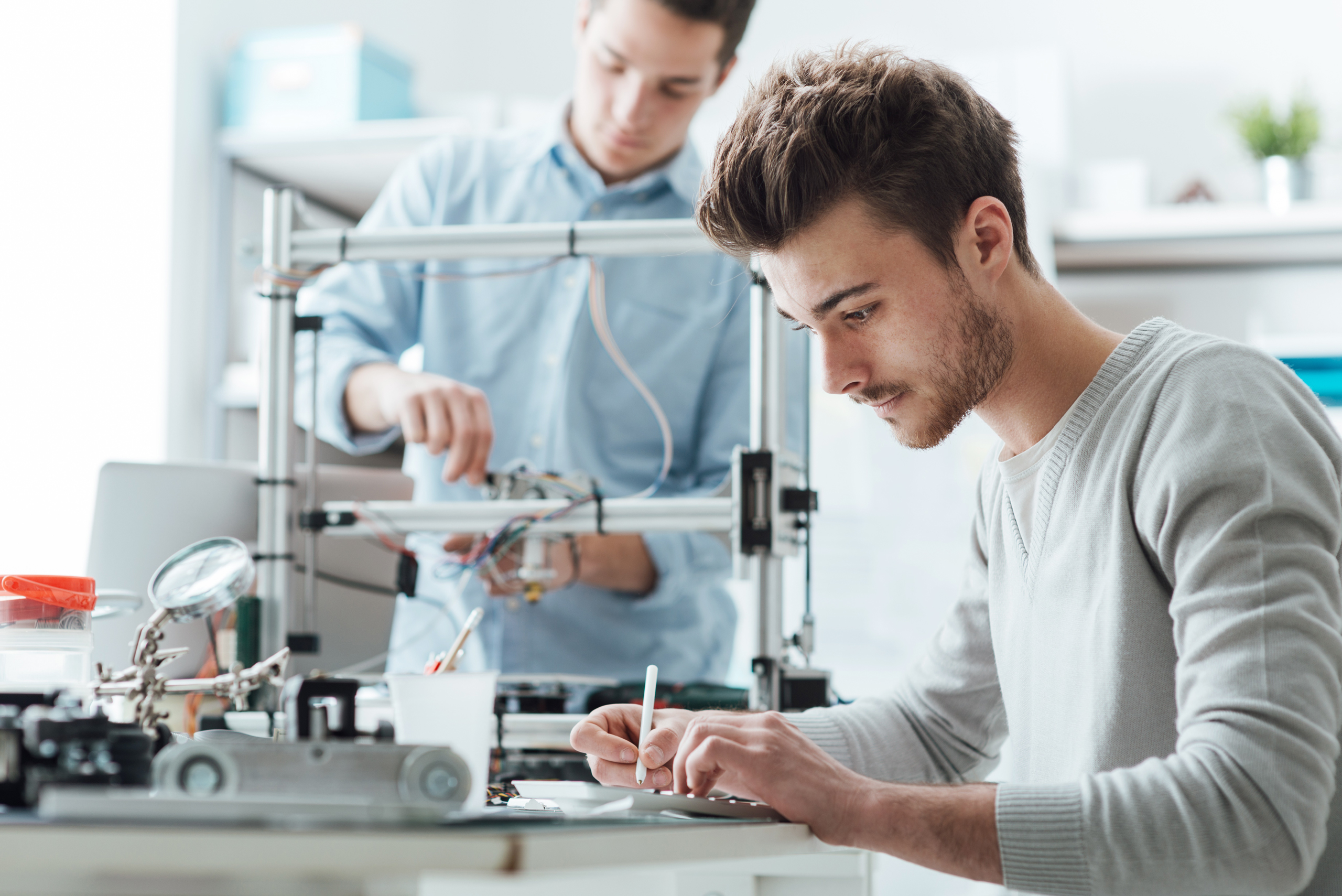 Ingenieurstudenten arbeiten im Labor, im Hintergrund benutzt ein Student einen 3D-Drucker
